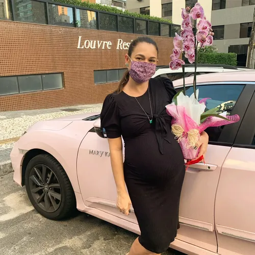 Consultora grávida ao lado do seu carro rosa Mary Kay